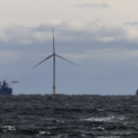 Image of a wind turbine in the ocean with a large ship in the background