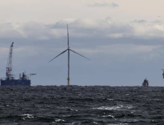 Image of a wind turbine in the ocean with a large ship in the background