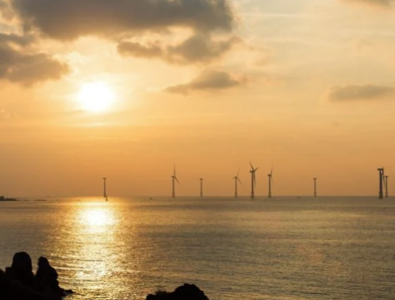 a scenic view of the ocean in the late afternoon with a group of wind turbines visible in the distance